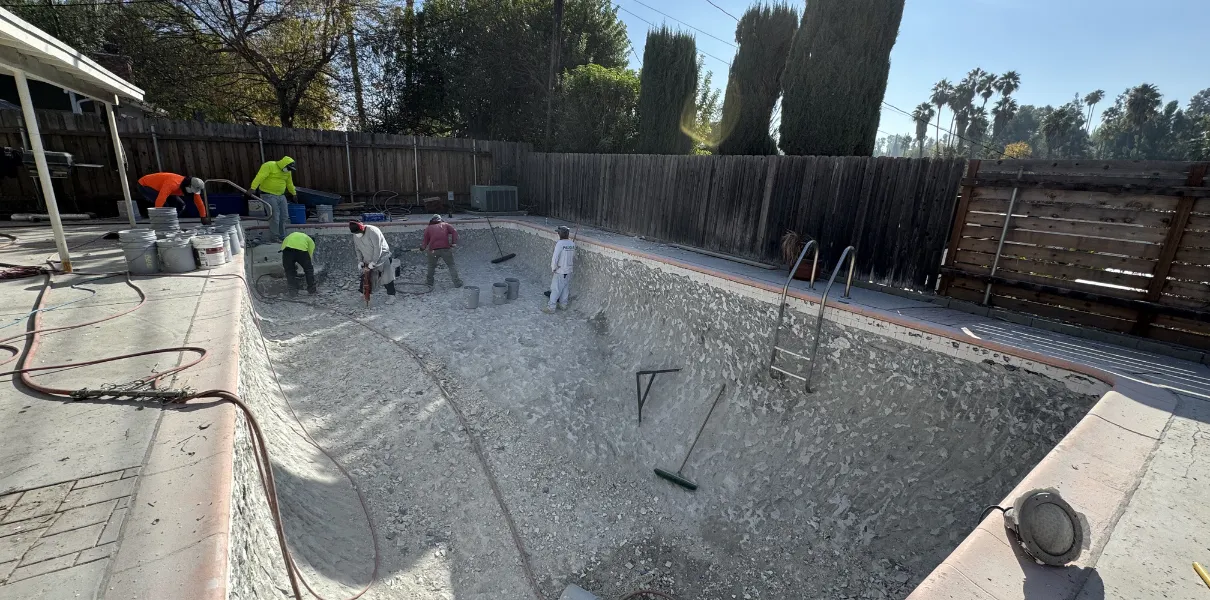 A wide, sunlit view of an older backyard swimming pool in Los Angeles, showing wear on the plaster, tile line, and some remaining green water, ready for a complete remodeling and renovation.
