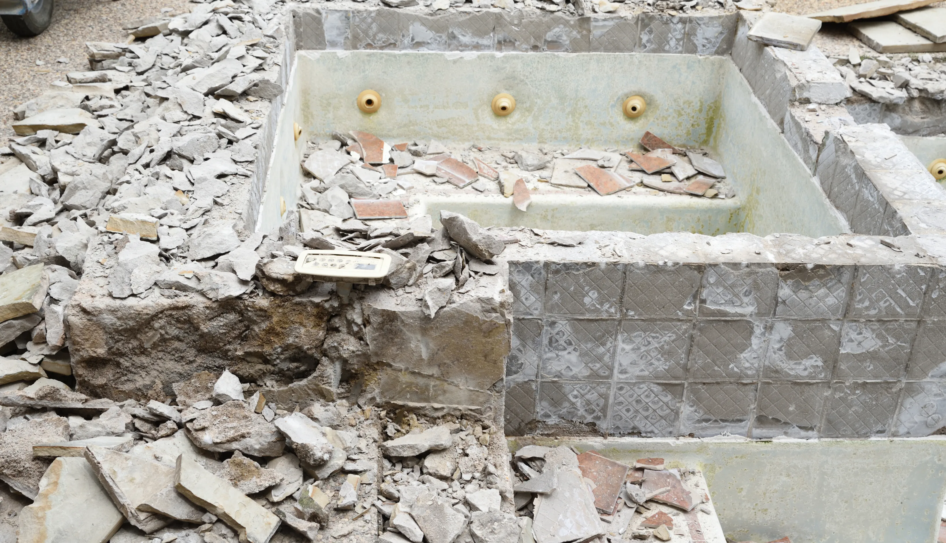 A severely damaged backyard pool in Los Angeles during the initial demolition phase, showing broken concrete and structural debris.